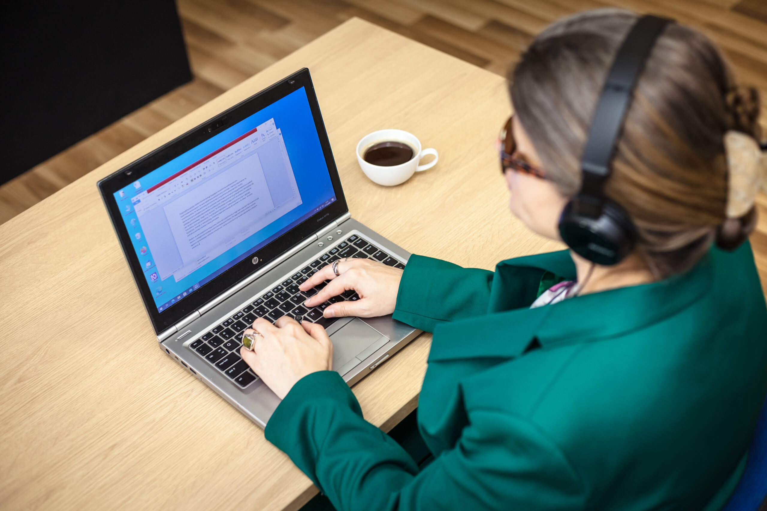 Niewidoma kobieta w biurze siedząc przy biurku pisze na laptopie.